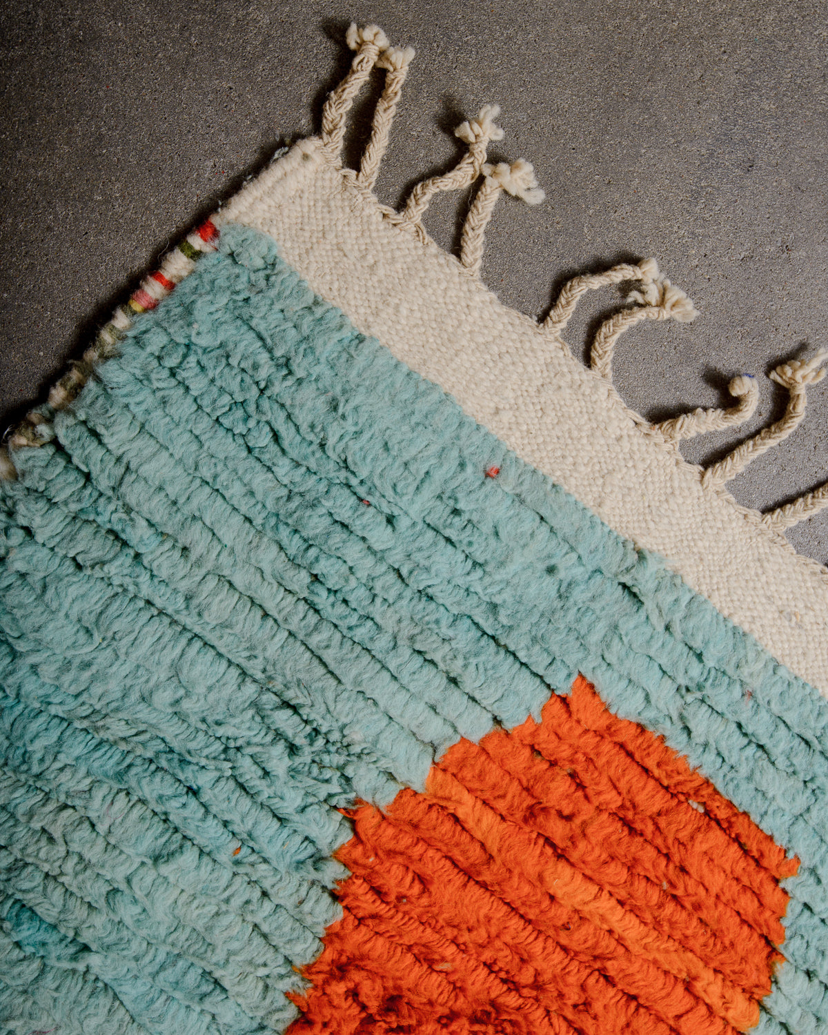 Corner of vintage berber rug with woven edge and natural wool tassels.